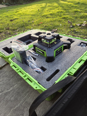 Grettz green rotary laser level in its open green moulded carry case on the ground outdoors, with accessories bag alongside