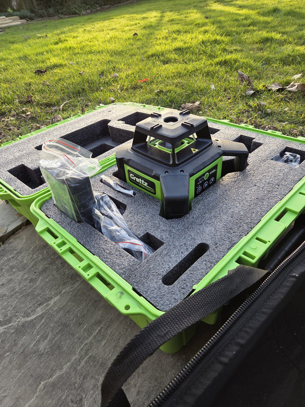 Grettz green rotary laser level in its open green moulded carry case on the ground outdoors, with accessories bag alongside