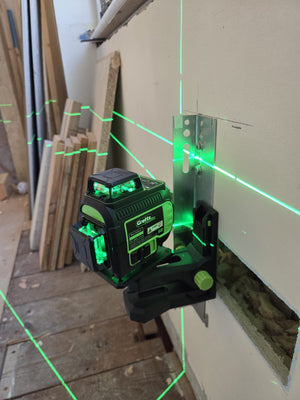 Grettz G4D green beam multi-line laser mounted on a wall bracket projecting bright green horizontal and vertical laser lines across an interior first-fix room with timber